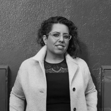 Black and white photo of Tina Gharavi standing against a wall.