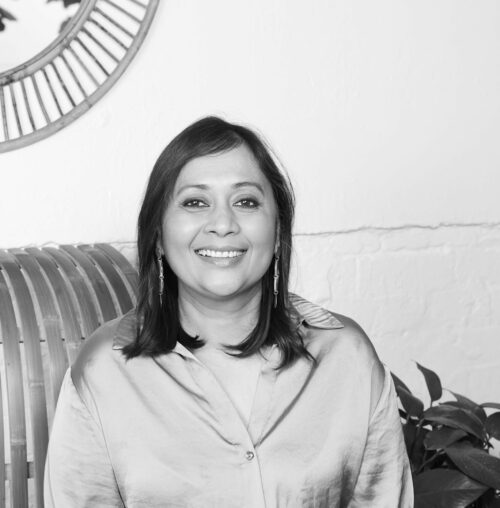 Black and white photo of Pragya Agarwal sitting on a sofa, smiling.